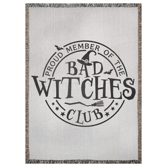 A 37x52 inch woven blanket depicting a Halloween emblem that says "proud member of the bad witches club". It has bats, a broomstick, and a witch's hat. 