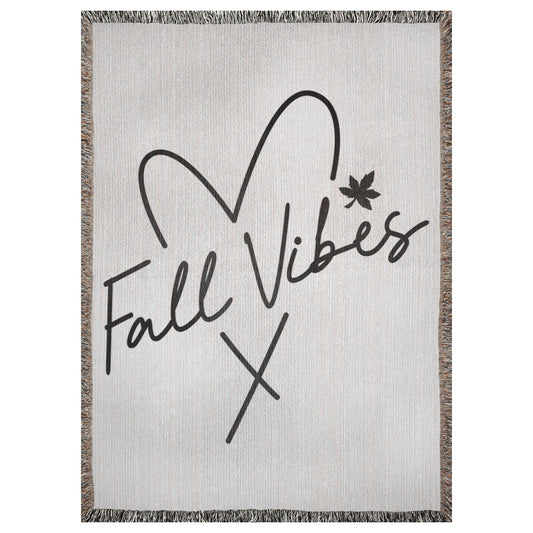 A 37x52 inch woven blanket depicting the outline of a heart with the words "fall vibes" written through the middle of the heart. There is also an autumn leaf.